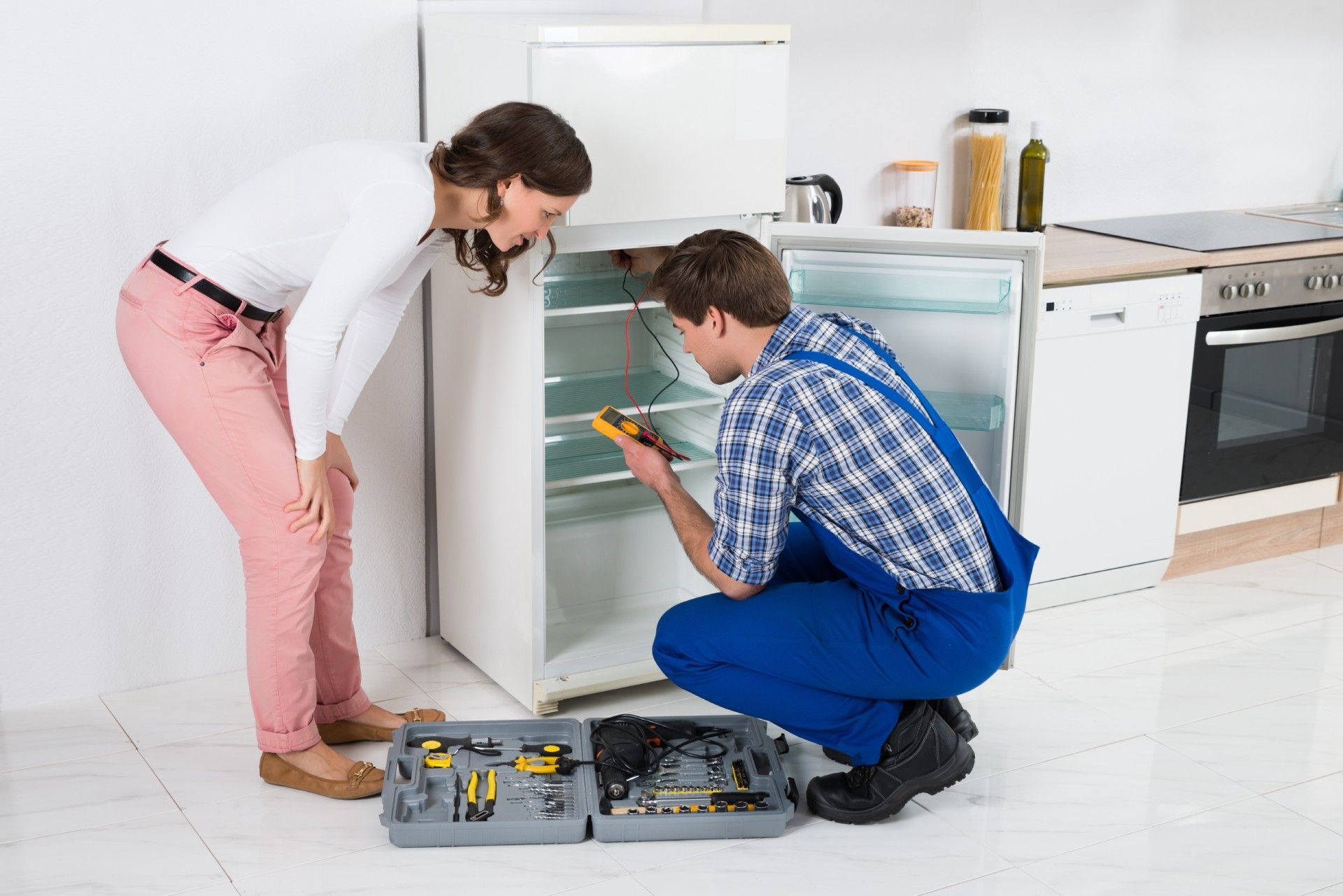 A man and a woman are fixing a refrigerator in a kitchen.