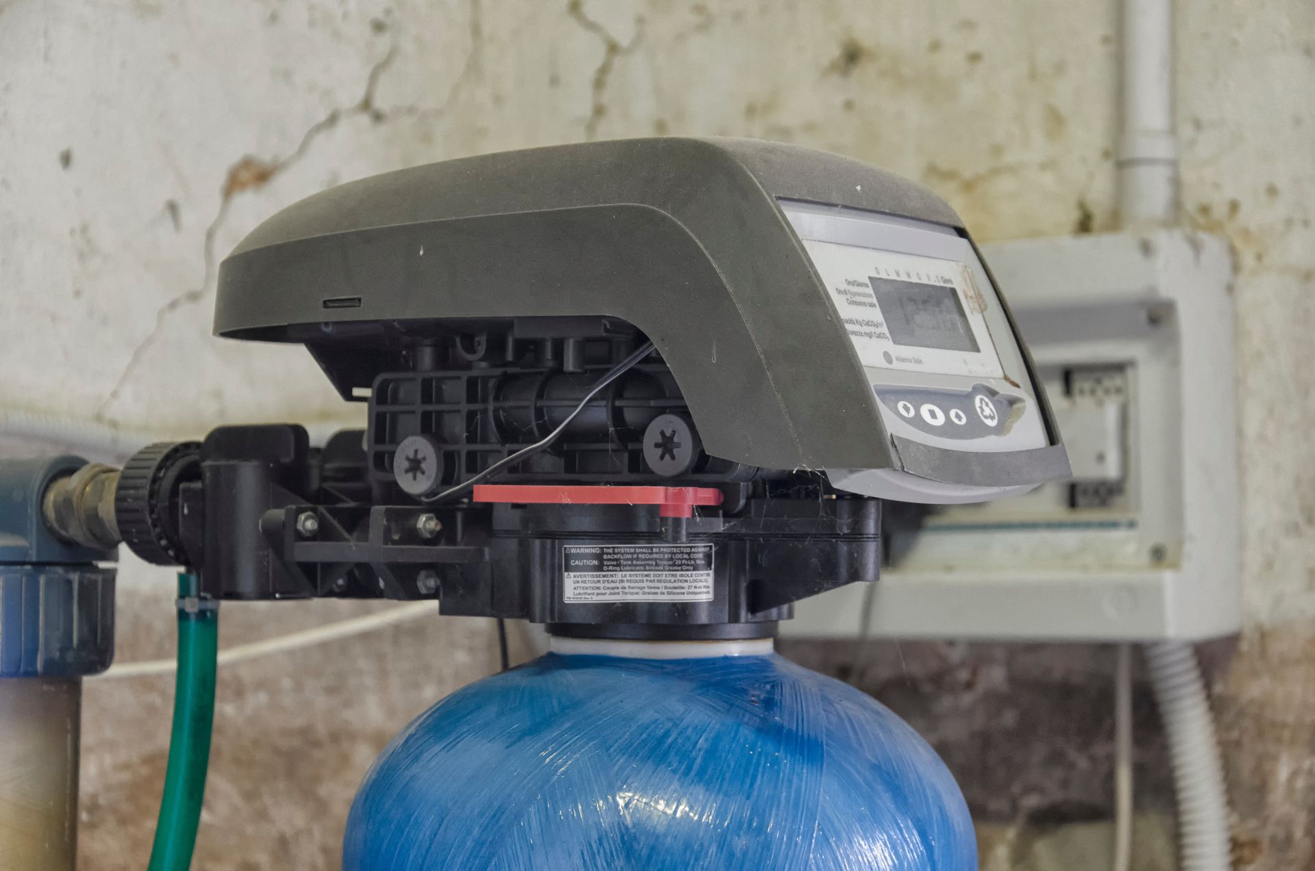 Water softener control head on a blue tank, mounted against a wall with hoses attached.