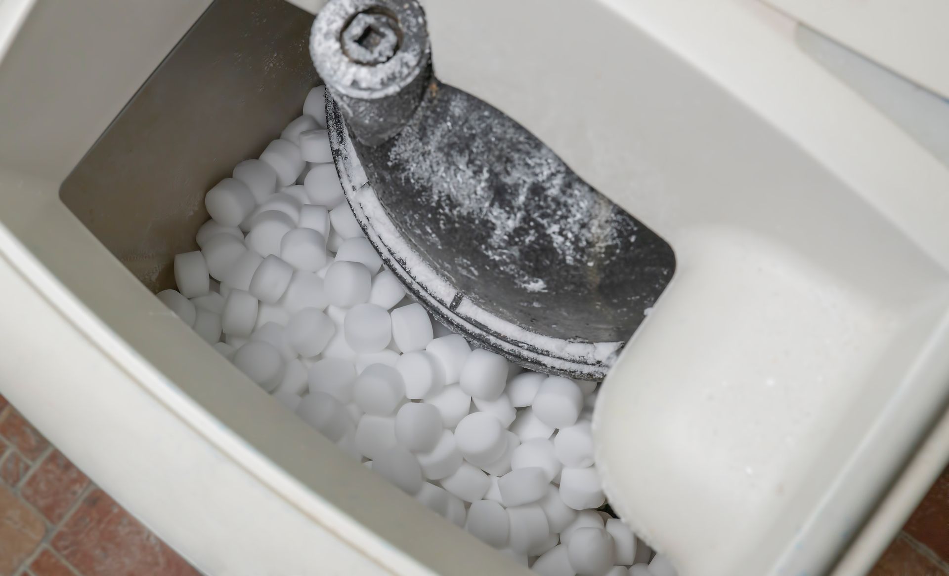 Top view of an ice maker bin filled with ice, showing the frosted metal auger inside.