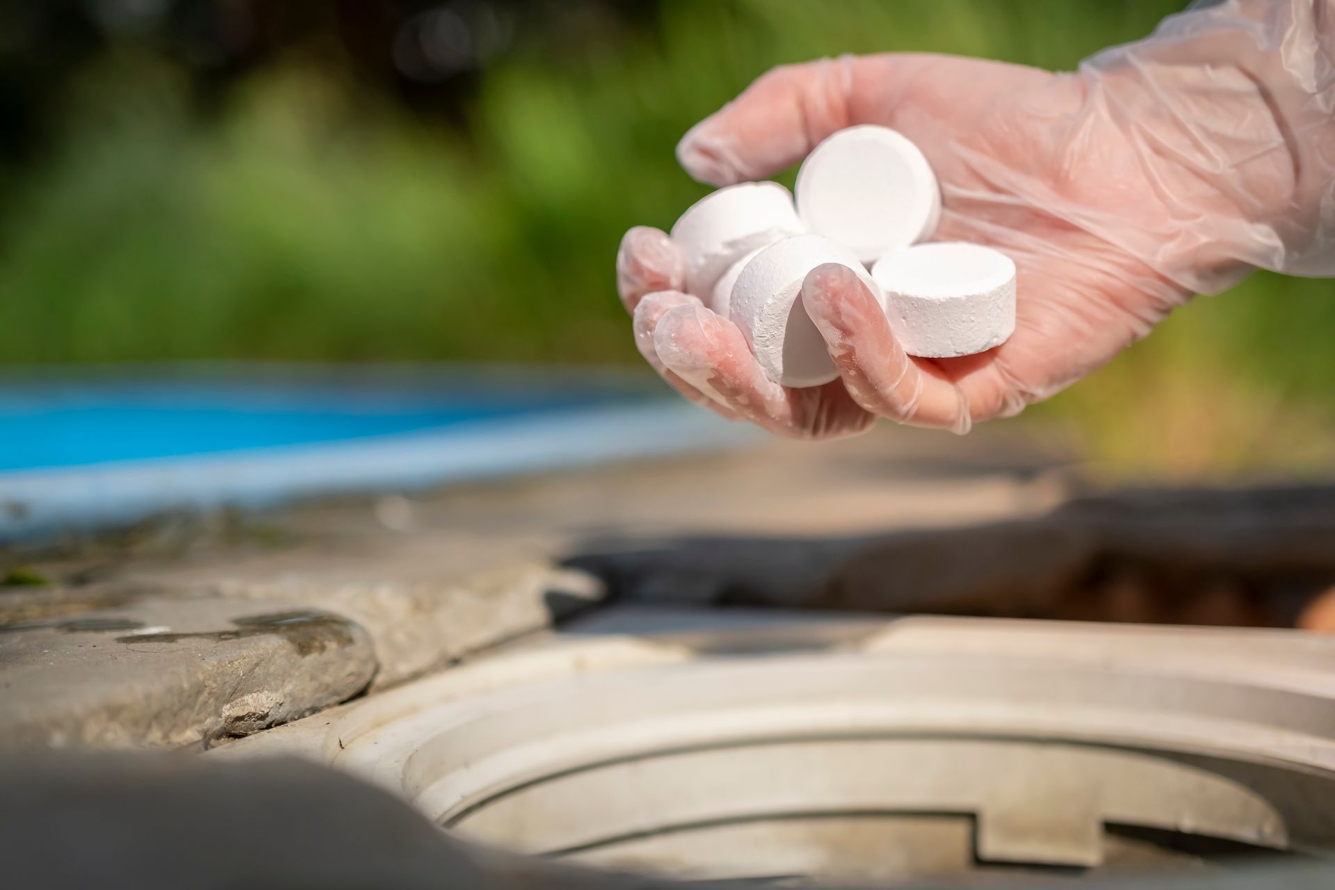 Hand placing white chlorine tablets into a pool skimmer basket
