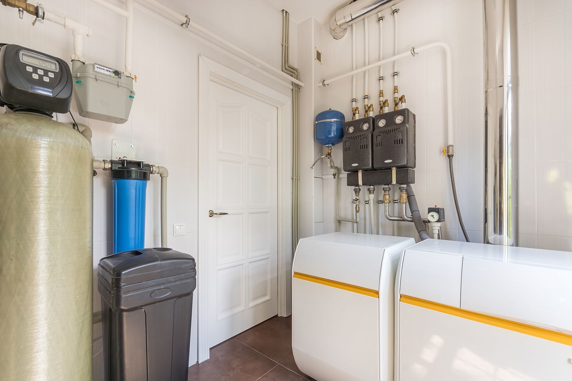 Utility room with water tanks, filters, pipes, and a closed white door