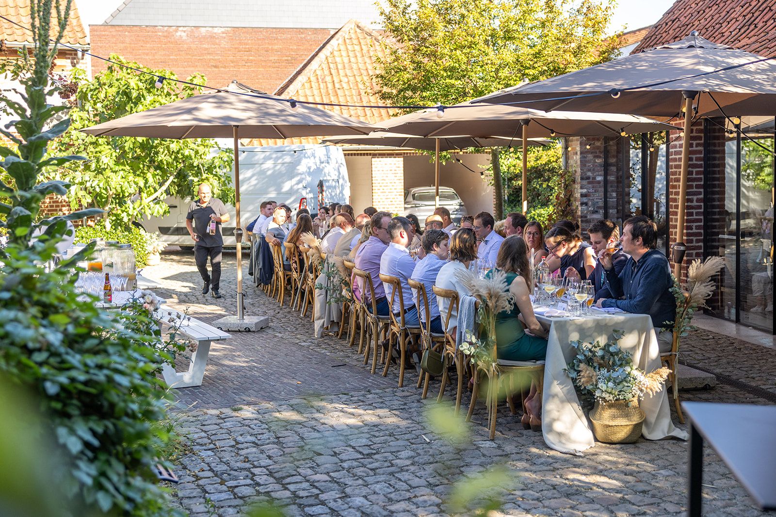 Pasgetrouwden lopen hand in hand door het hoge gras. De vrouw draagt een witte jurk. De man een pak. Ze glimlachen.