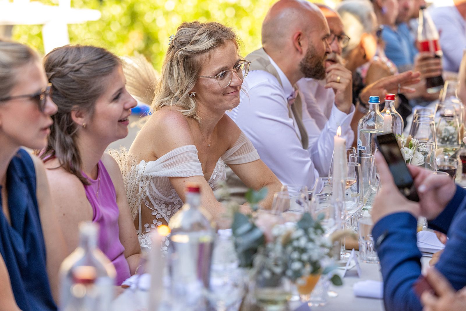 Een stel kust elkaar tijdens een strandbruiloft. De bruid draagt een witte jurk, de bruidegom een grijs pak, en de zon schijnt.