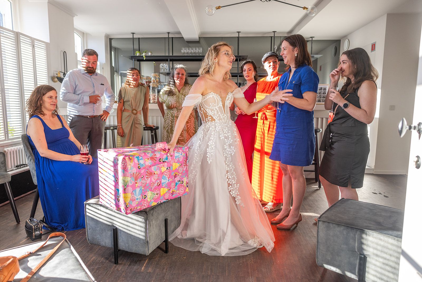 Een stel omhelst elkaar op het strand; de vrouw in de witte jurk houdt een boeket vast, de man in het beige pak raakt haar gezicht aan, met de oceaan op de achtergrond.