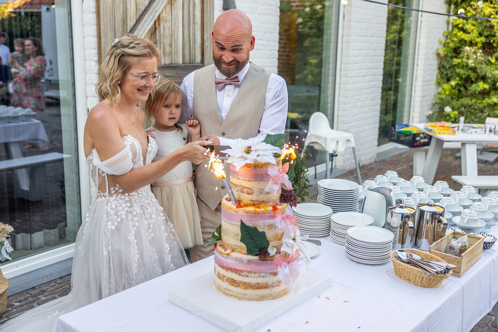 Een bruidspaar kijkt elkaar aan op een nat strand, hun spiegelbeeld in het ondiepe water.
