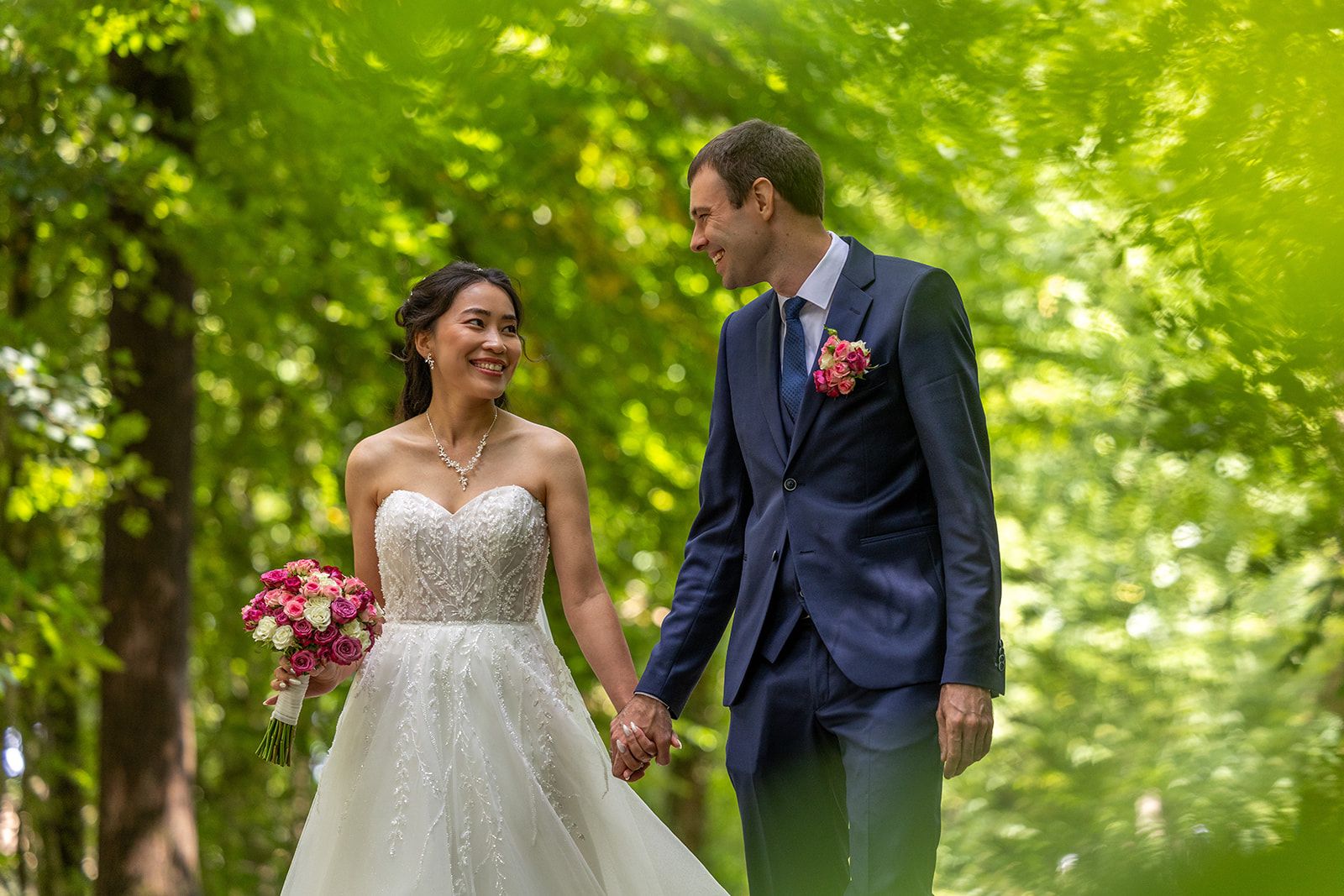 Een stel kust elkaar tijdens een strandbruiloft. De bruid draagt ​​een witte jurk, de bruidegom een ​​grijs pak, en de zon schijnt.
