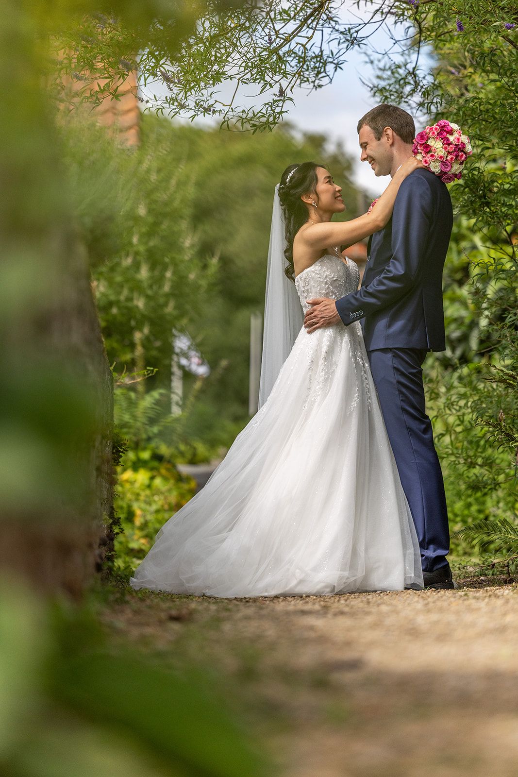 Een bruidspaar kijkt elkaar aan op een nat strand, hun spiegelbeeld in het ondiepe water.