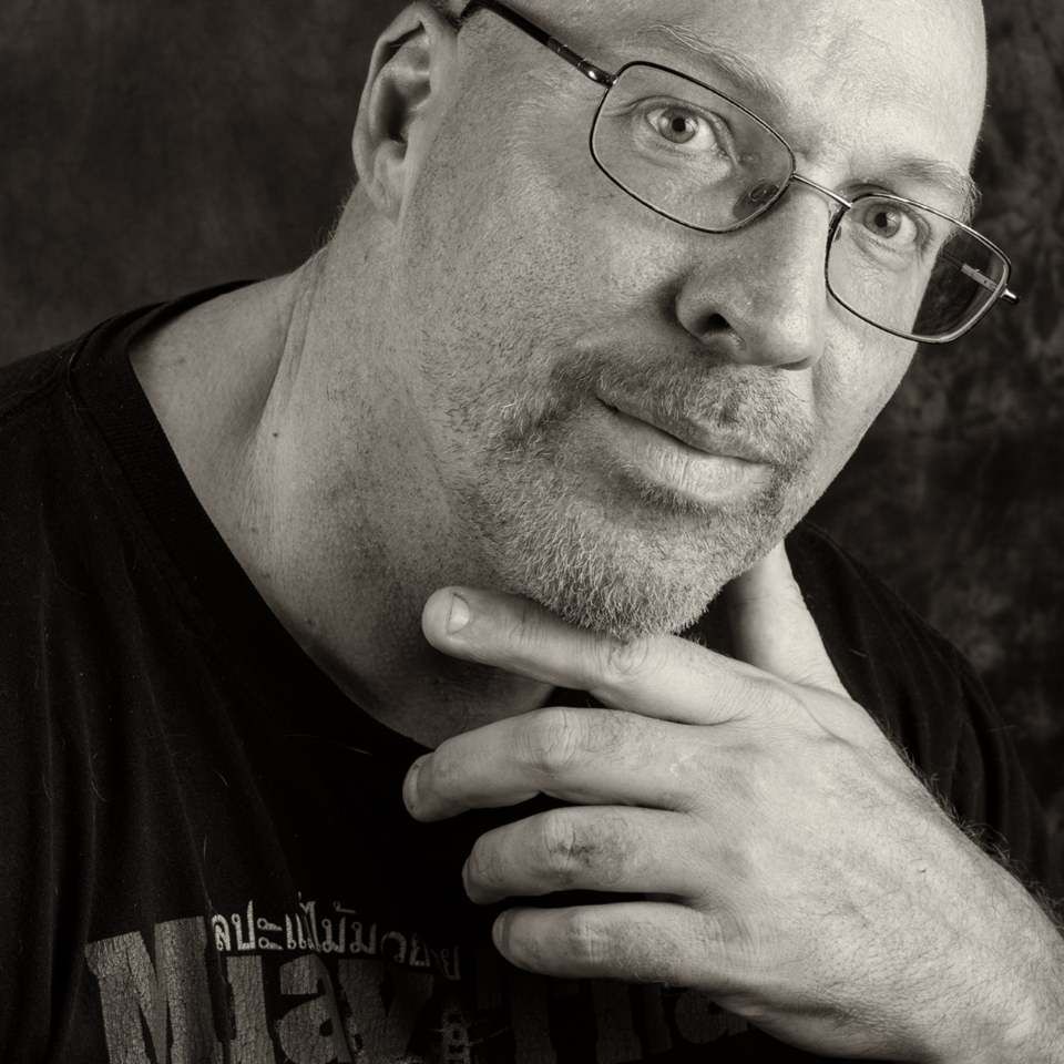Man met bril, hand op kin, kijkend naar de camera, zwart-witportret.
