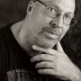 Man met bril, hand op kin, kijkend naar de camera, zwart-witportret.