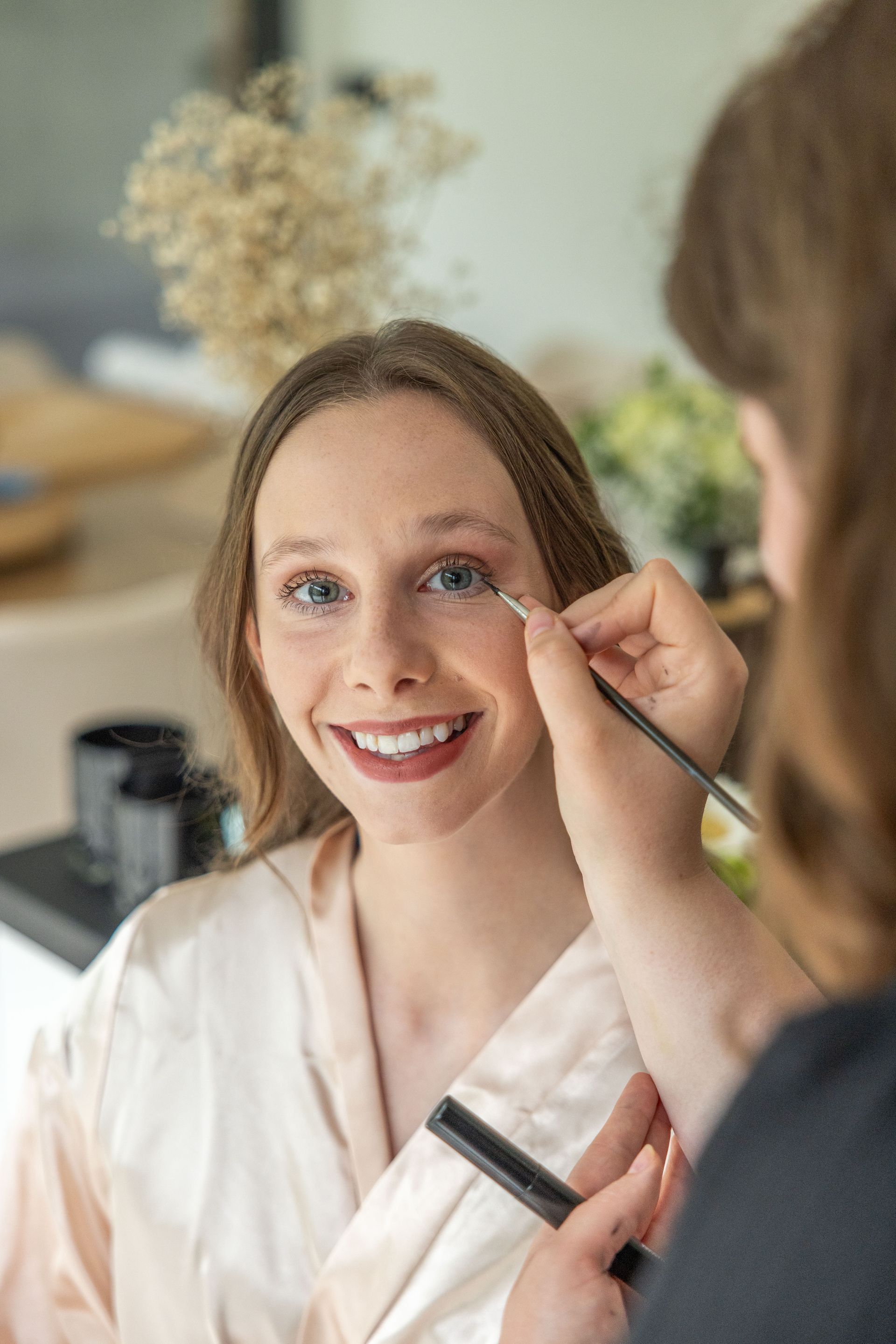 Vrouw lacht terwijl iemand anders haar make-up aanbrengt.