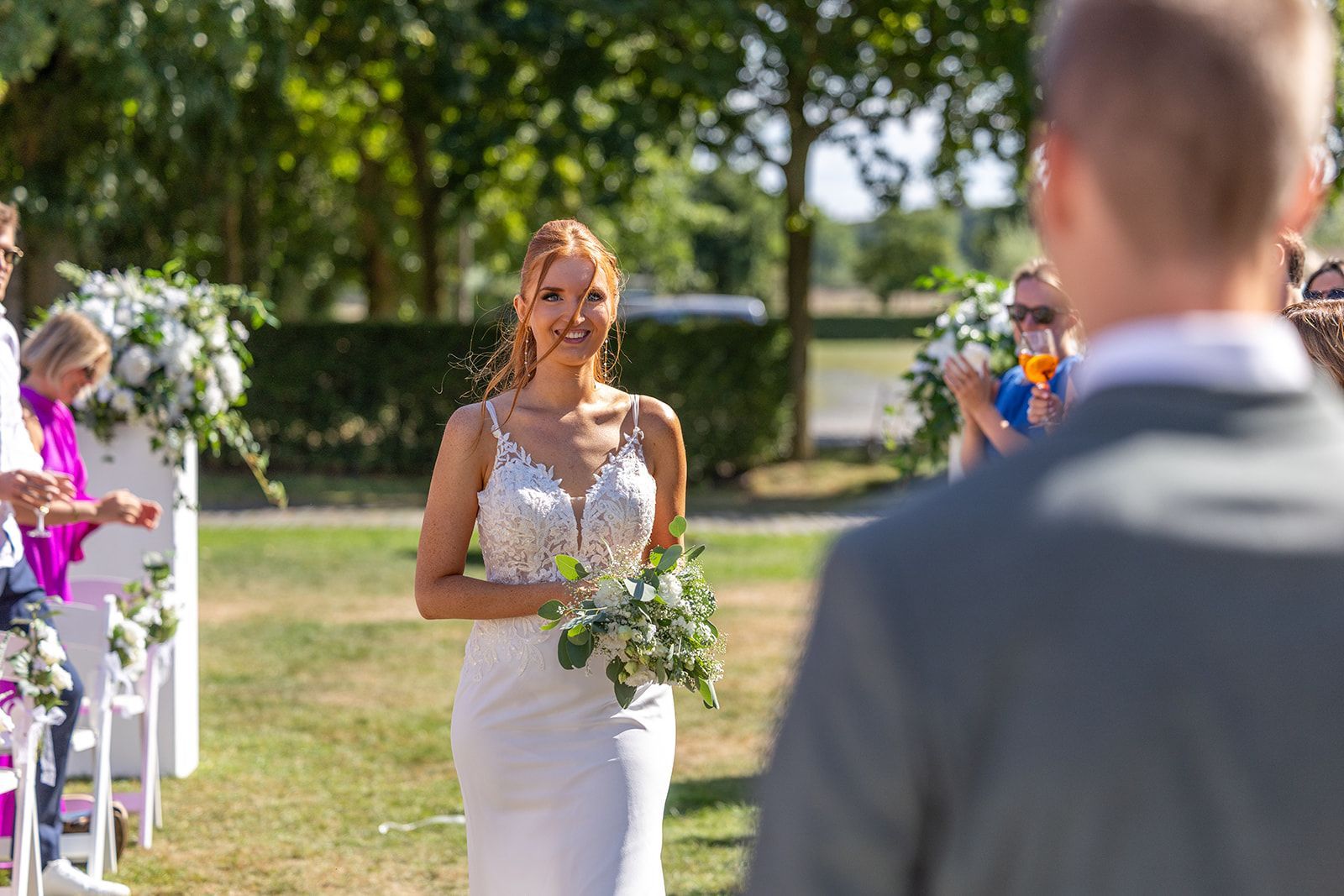 Bruid in witte jurk loopt naar bruidegom buiten tijdens huwelijksceremonie.