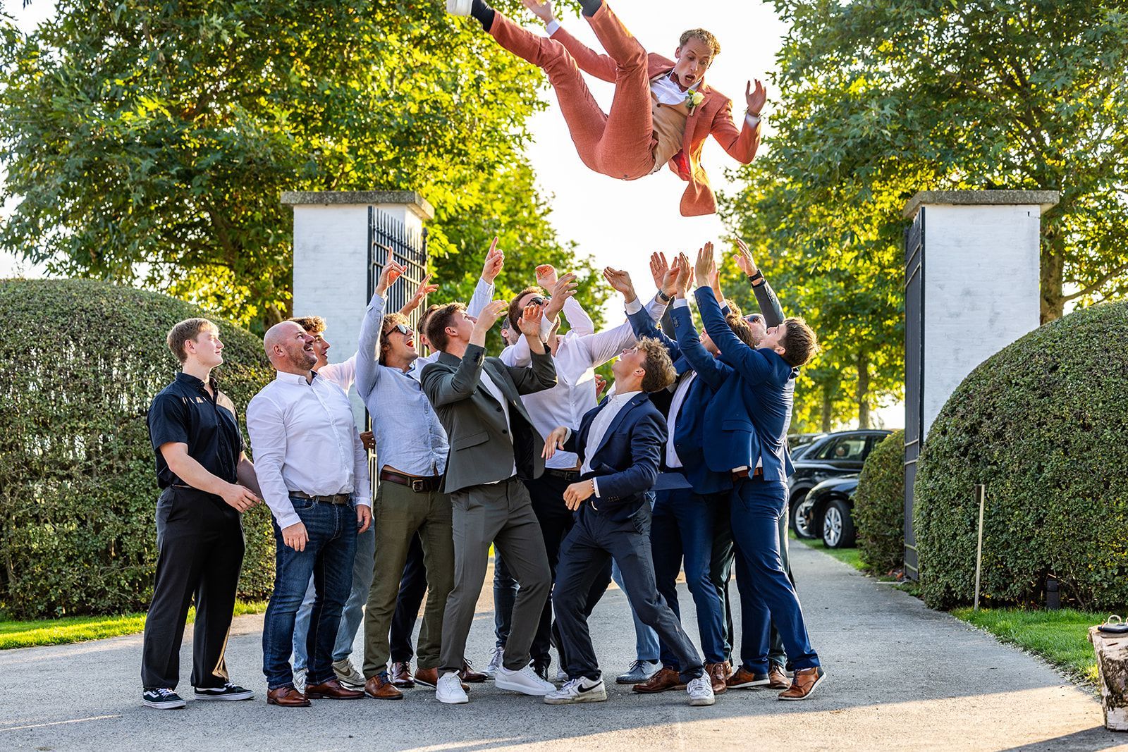 Mannen in pak gooien een andere man in de lucht; bruiloft in de buitenlucht.