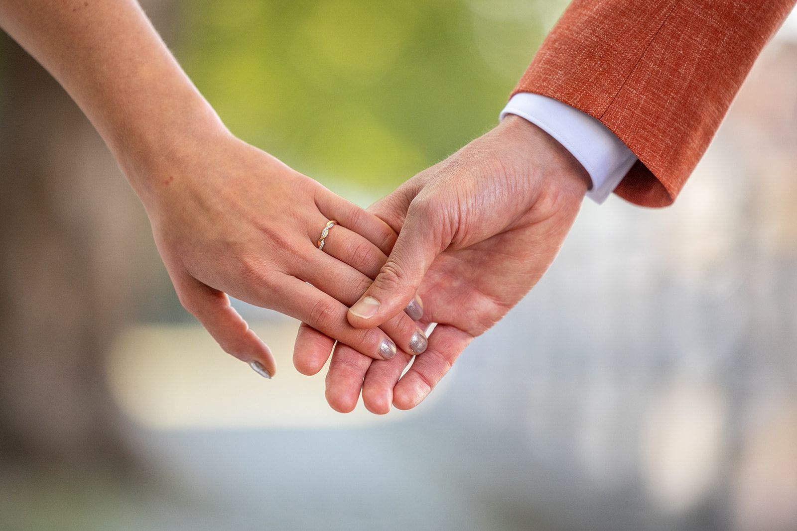 Een stel hand in hand, een van hen draagt ​​een ring. Een man draagt ​​een bruin pak. Buiten, zachte achtergrond.