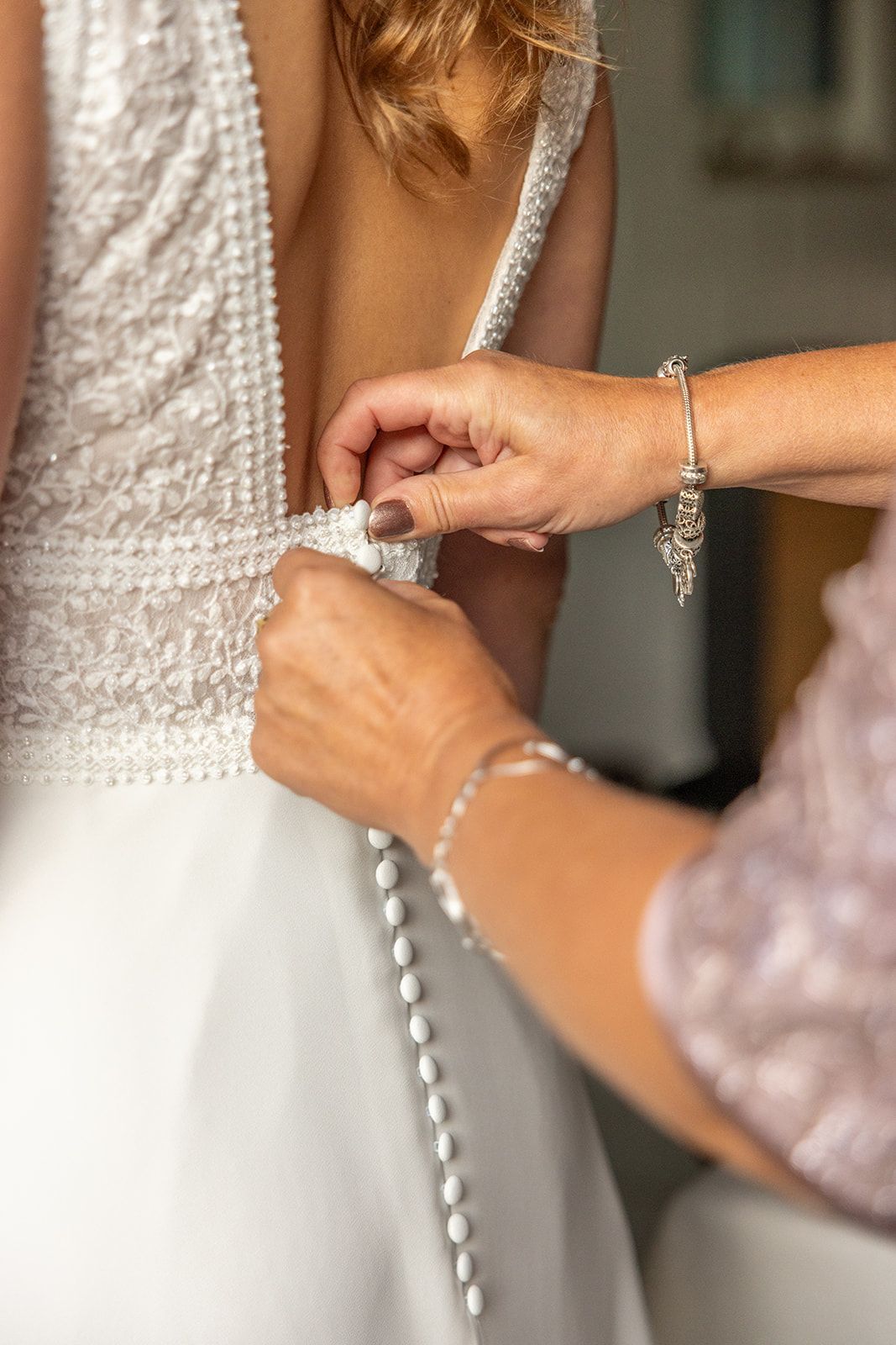 De trouwjurk van een vrouw wordt dichtgeknoopt door iemand anders. Close-up toont details op de rug.