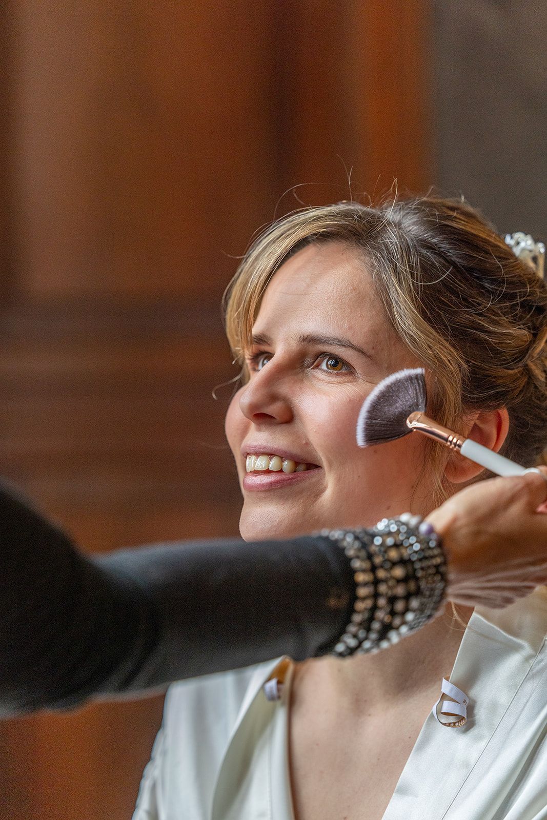 Vrouw die met een kwast make-up opdoet; lachend in een wit gewaad.