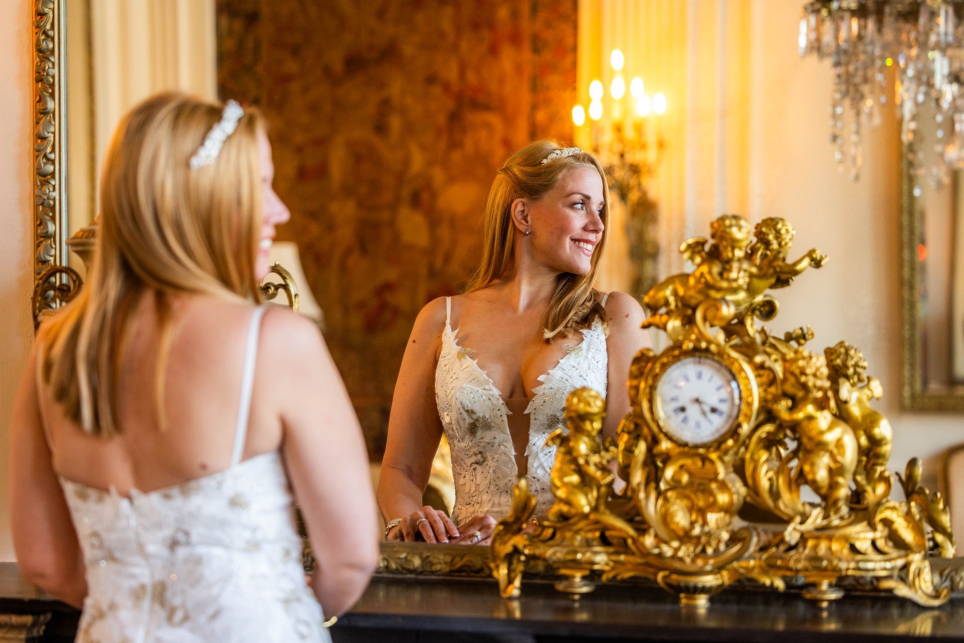 Bruid kijkt in de spiegel. Een andere bruid staat met haar gezicht van haar af. Sierlijke gouden klok op tafel. Elegante kamer, zachte verlichting.
