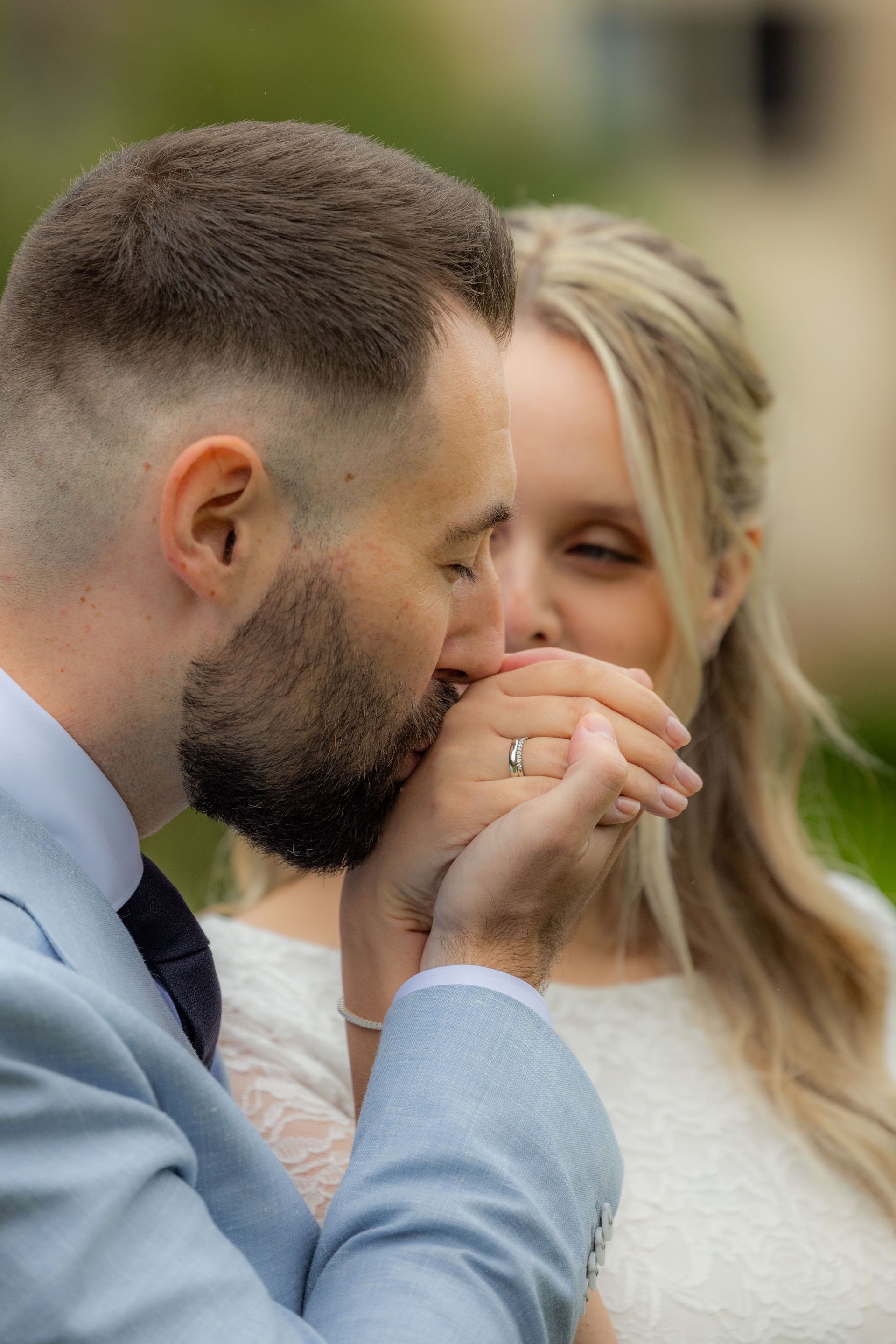 Man kust de hand van vrouw. Hij draagt ​​een lichtblauw pak. Zij draagt ​​een witte jurk. Buiten, wazige achtergrond.