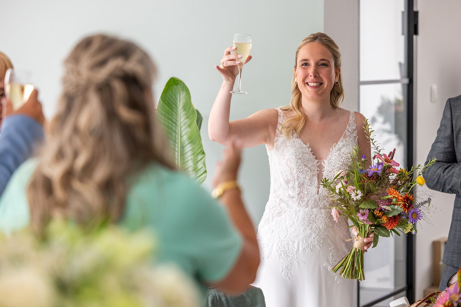 Bruid in witte jurk heft het glas champagne; gasten toosten.