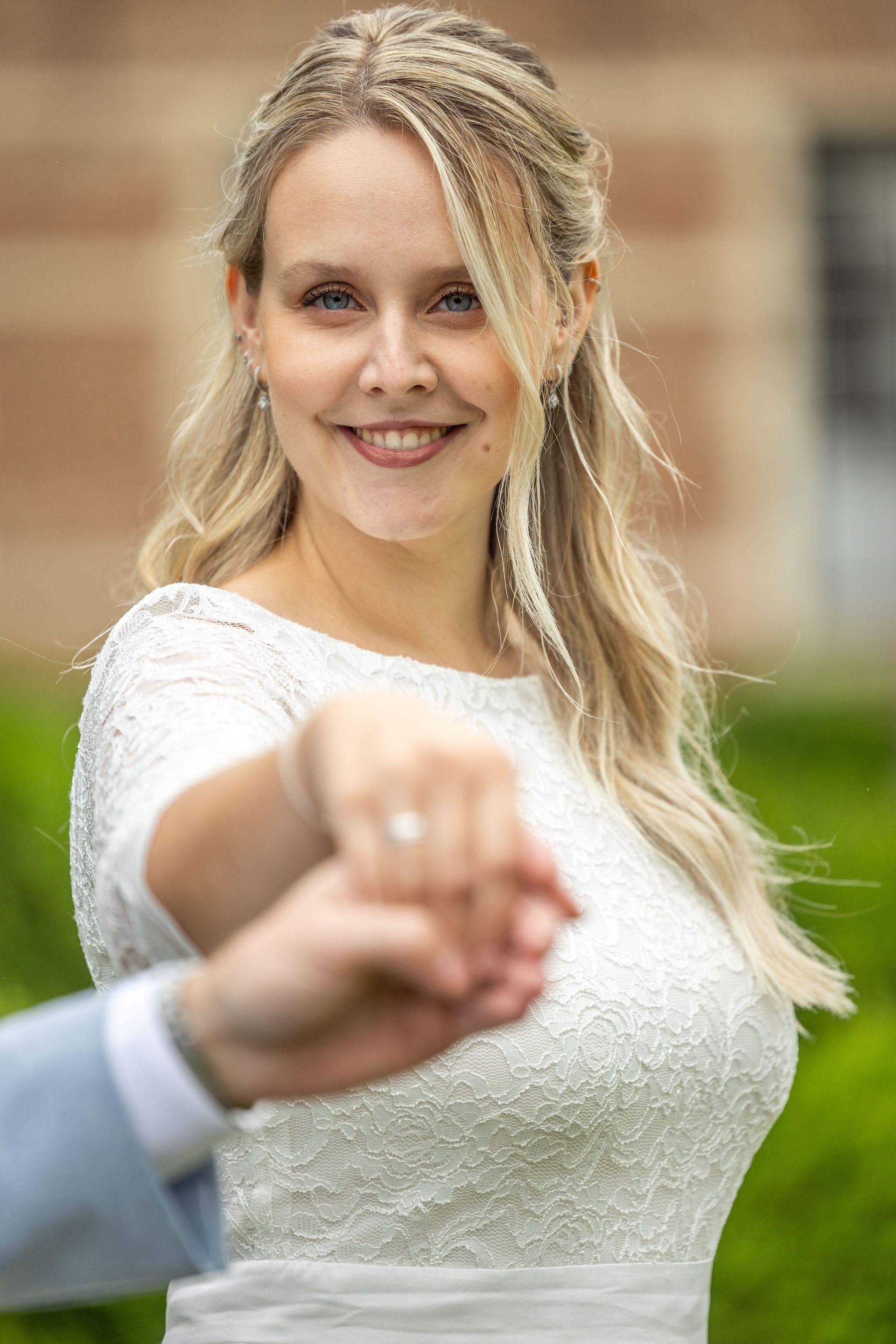Vrouw in trouwjurk steekt glimlachend haar hand uit, buiten.
