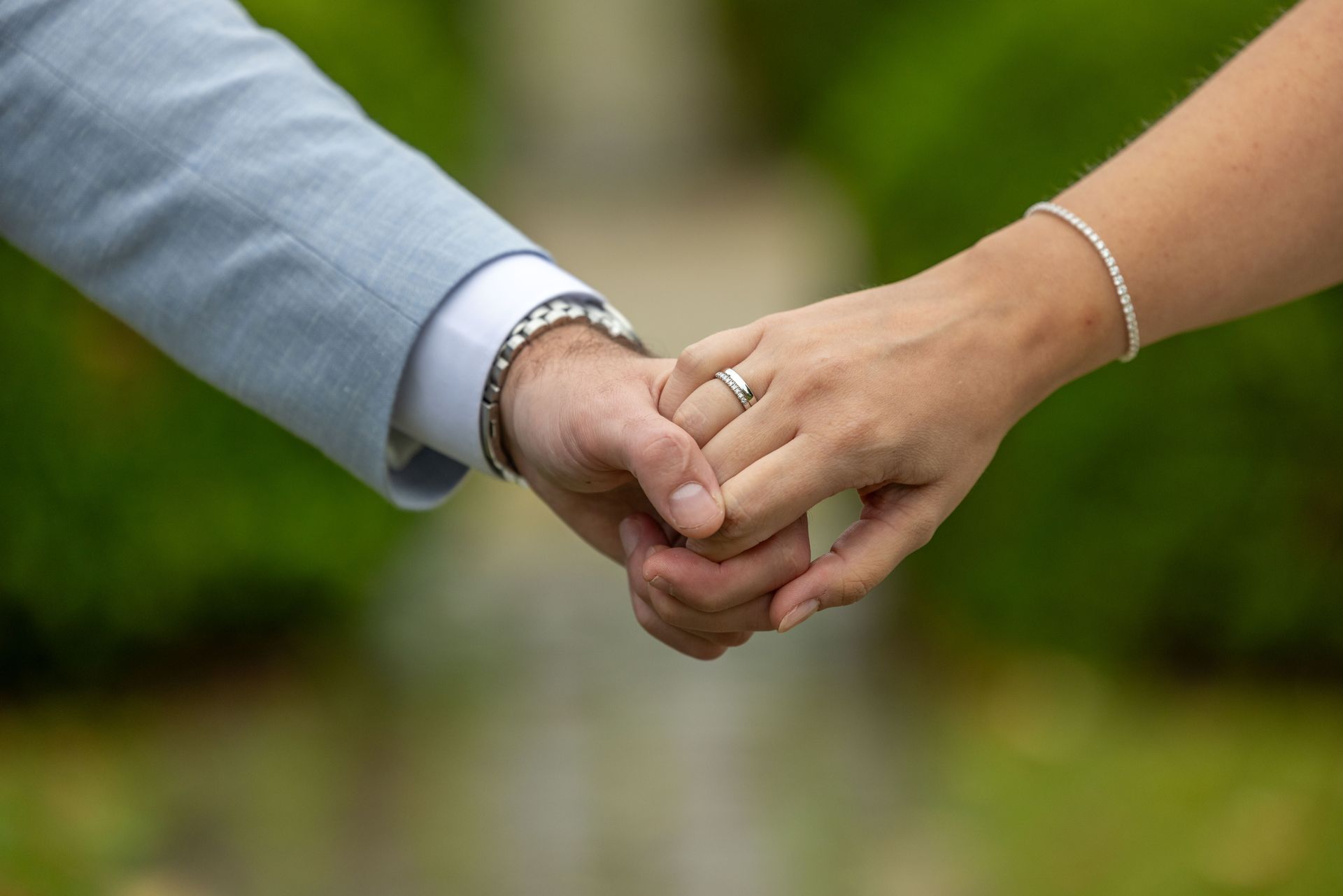 Twee mensen hand in hand, de een in pak en de ander met een armband. Trouwring zichtbaar.