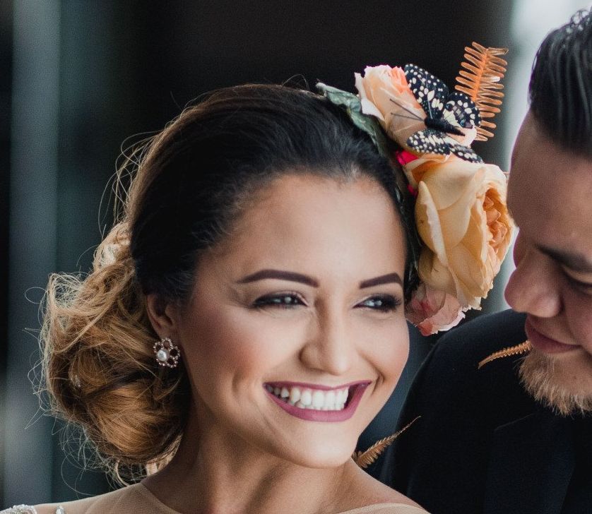 Lachende vrouw met bloemenhoofdtooi naast persoon in pak, beiden binnen.