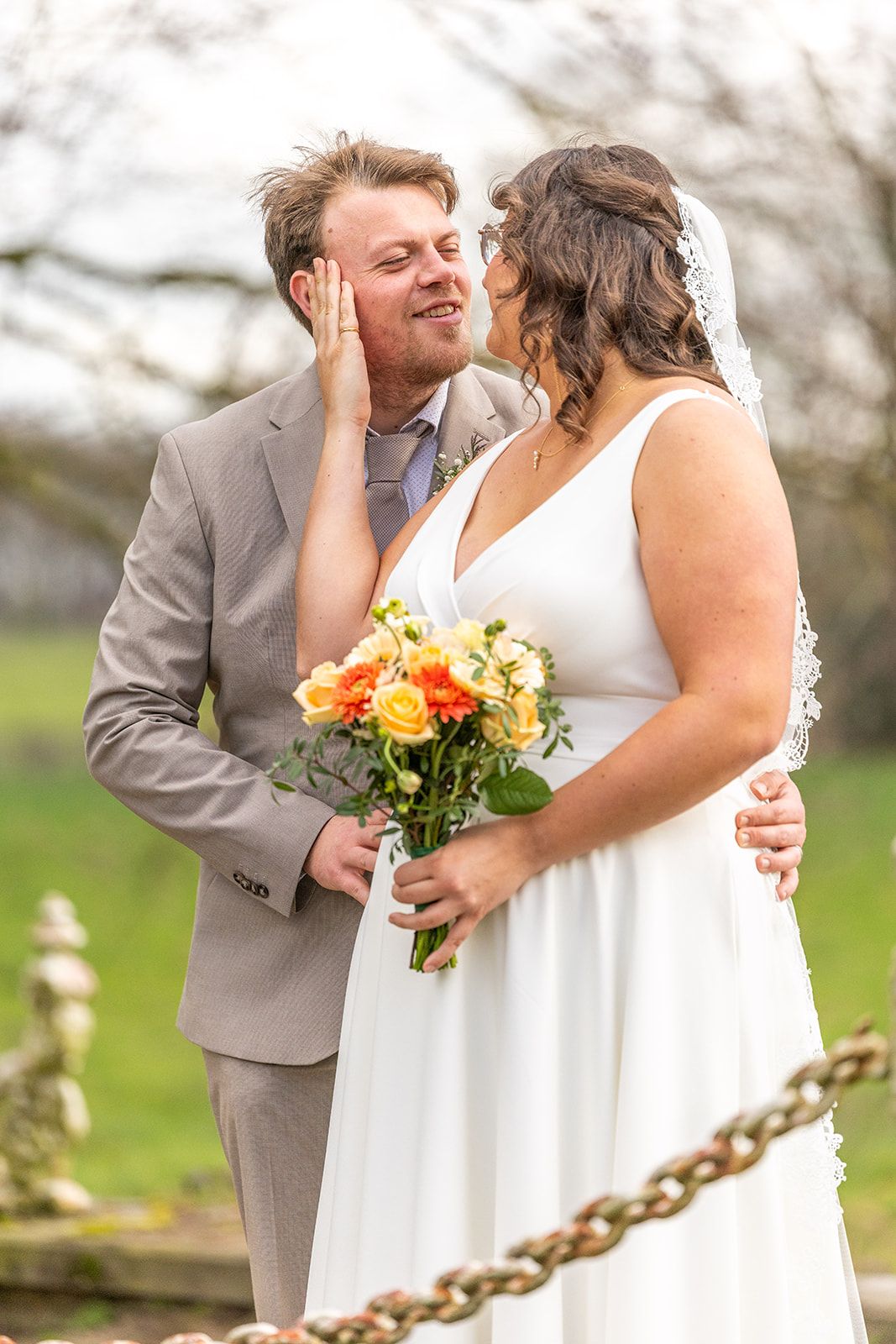 Een bruidspaar kijkt elkaar aan op een nat strand, hun spiegelbeeld in het ondiepe water.