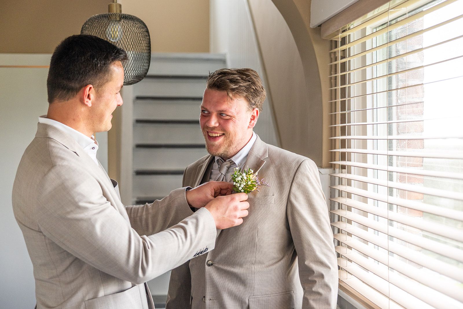 Pasgetrouwden lopen hand in hand door het hoge gras. De vrouw draagt ​​een witte jurk. De man een pak. Ze glimlachen.