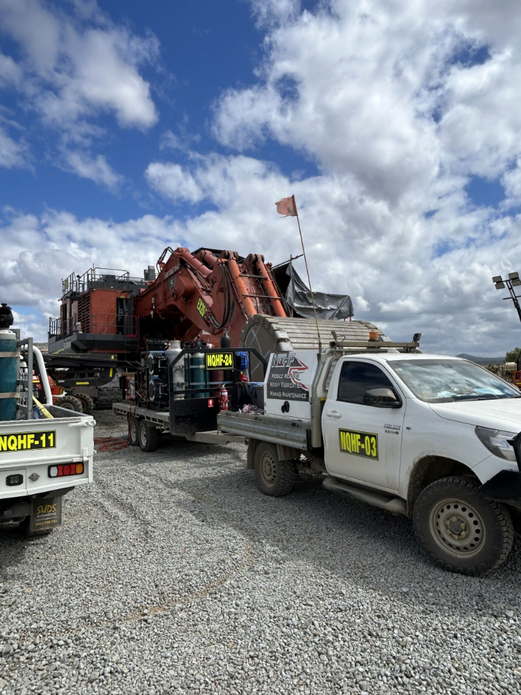 Heavy equipment excavator on trailer next to a white service truck under a cloudy sky— North Queensland Hard Facing (NQHF) In Fredericksfield, QLD