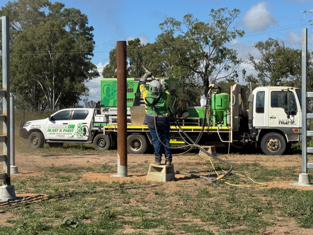 Worker sandblasting a metal post outdoors, near trucks and a gate. — North Queensland Hard Facing (NQHF) In Fredericksfield, QLD