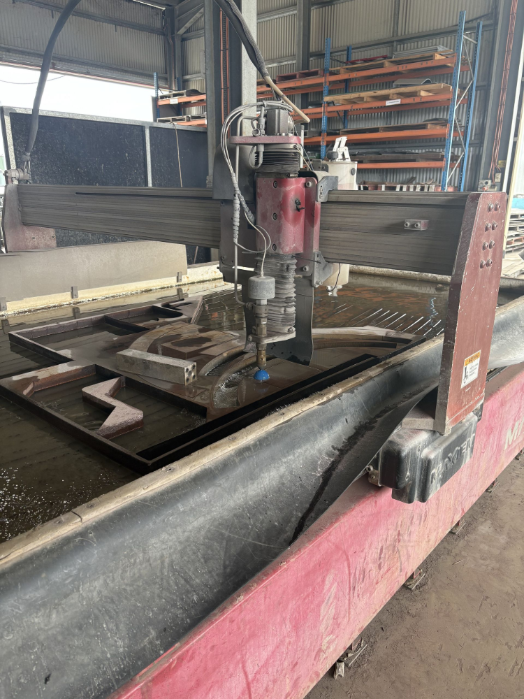 Water jet cutting machine processing metal sheets in a workshop, producing a patterned shape— North Queensland Hard Facing (NQHF) In Fredericksfield, QLD
