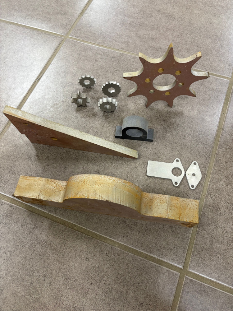 Assorted machine parts, including sprockets, gears, and a bearing. Beige and metallic tones on a tile floor— North Queensland Hard Facing (NQHF) In Fredericksfield, QLD