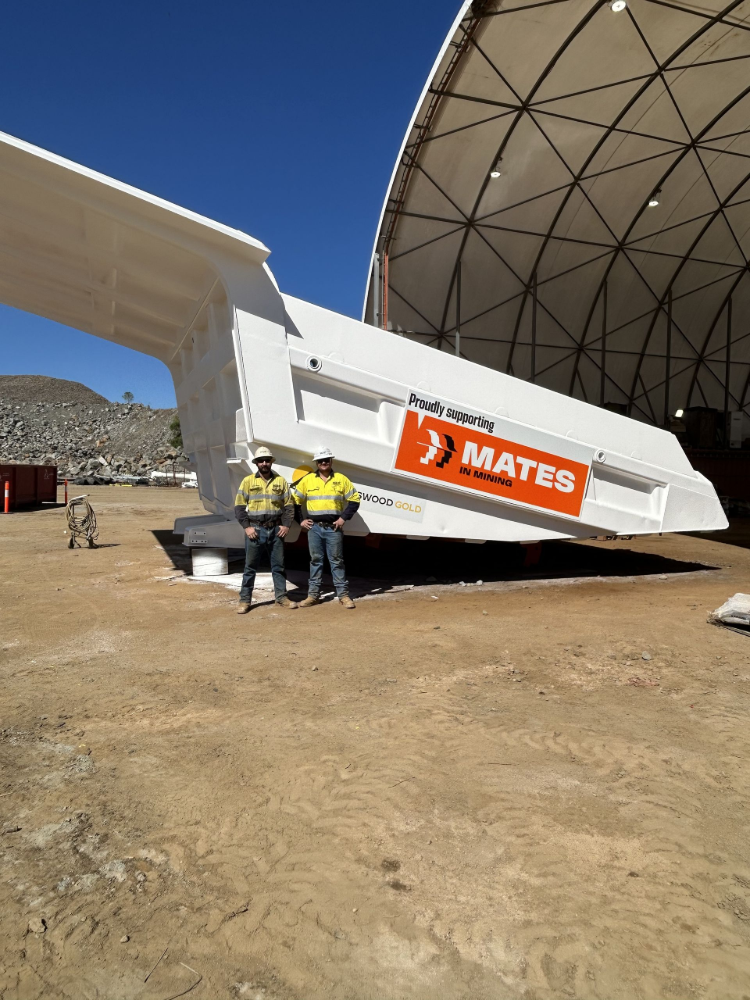 Two people stand near a large white construction component with