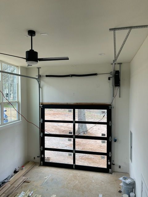Interior of a room with a modern glass garage door, a ceiling fan, and unfinished walls.