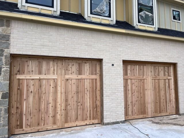 Two wooden garage doors on a light brick building. Two windows above are covered.