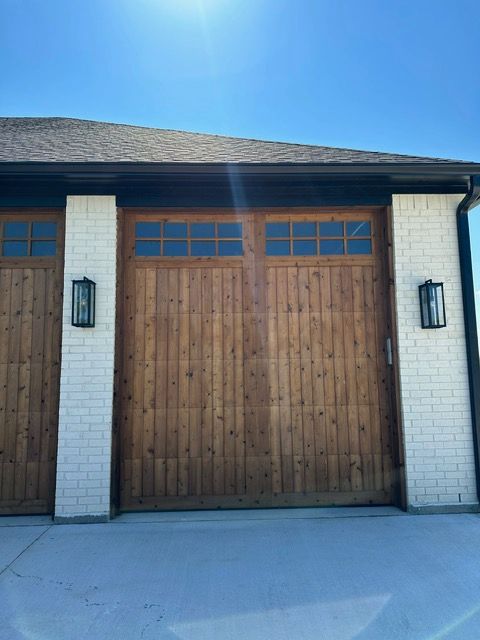 Wooden garage doors with glass windows set in brick columns, under a blue sky.
