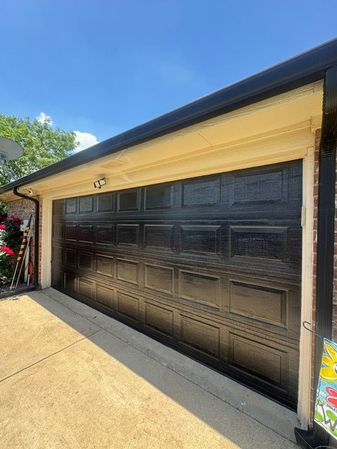 Black garage door under a beige overhang, set against a blue sky.