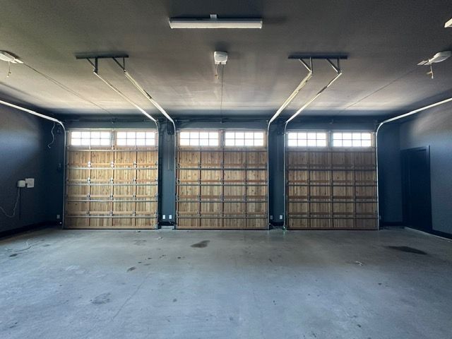 Three garage doors with window panes, wooden texture, inside a grey concrete garage.