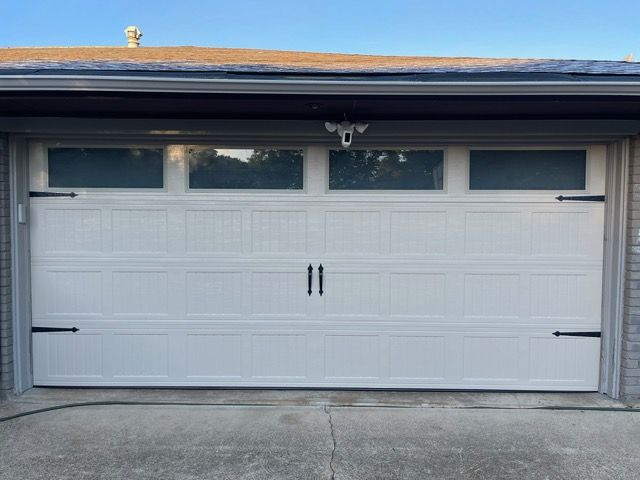 White garage door with three glass panes at the top, black hardware, and a security camera above.