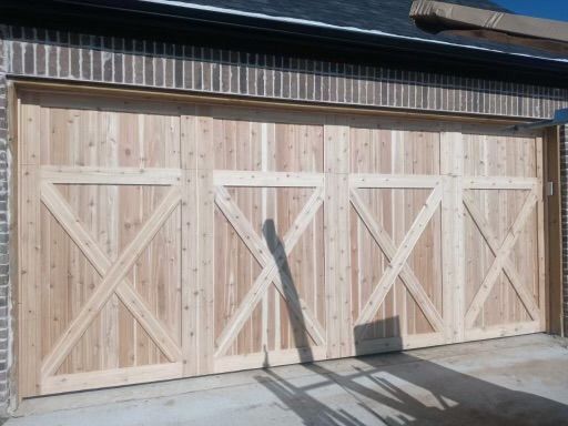 Light wood garage doors with an X design, set in a brick wall.