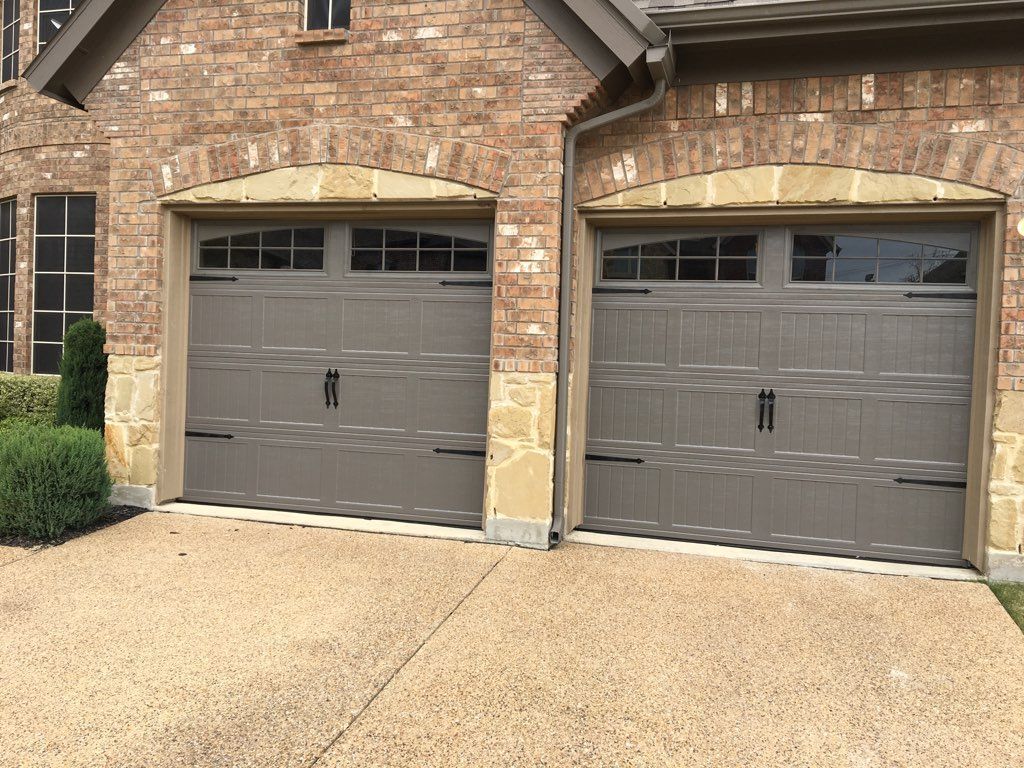 Two gray garage doors with decorative black hardware, set in a brick and stone facade.