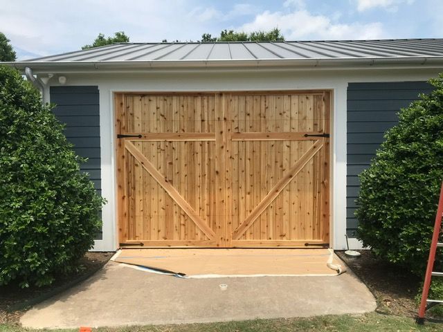 Wooden garage doors with diagonal supports on a blue building, bushes flank the entrance.