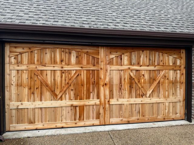 Wooden garage door with decorative arches and cross bracing, set against a dark roof and brown trim.