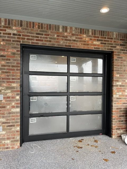 Black-framed glass garage door with eight panes, against a brick wall, on a gray gravel base.