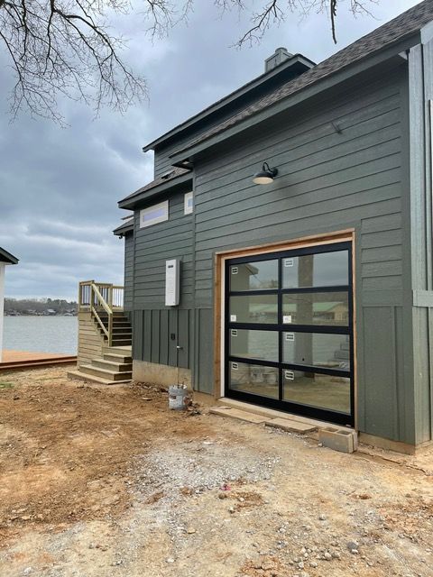 Modern home exterior with glass garage door, gray siding, and water view.