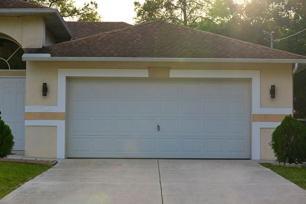Tan garage door on a tan house with a brown roof and a concrete driveway.