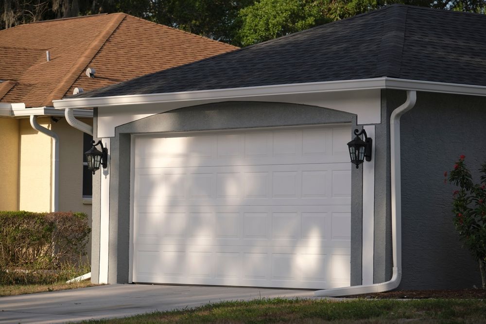 White garage door on a gray house, white trim, with brown roof visible.