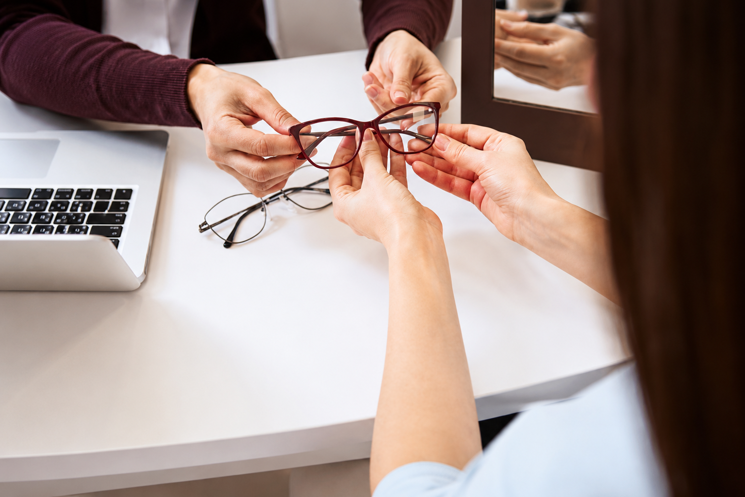 Hands reaching together to toast eyeglasses over a white table beside a laptop