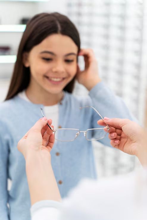 Optician holding eyeglasses for a smiling person in a bright exam room