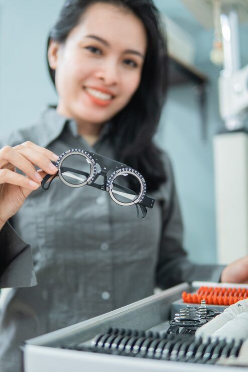 Woman holding black eyeglasses beside a display of eyeglass frames in an optical store