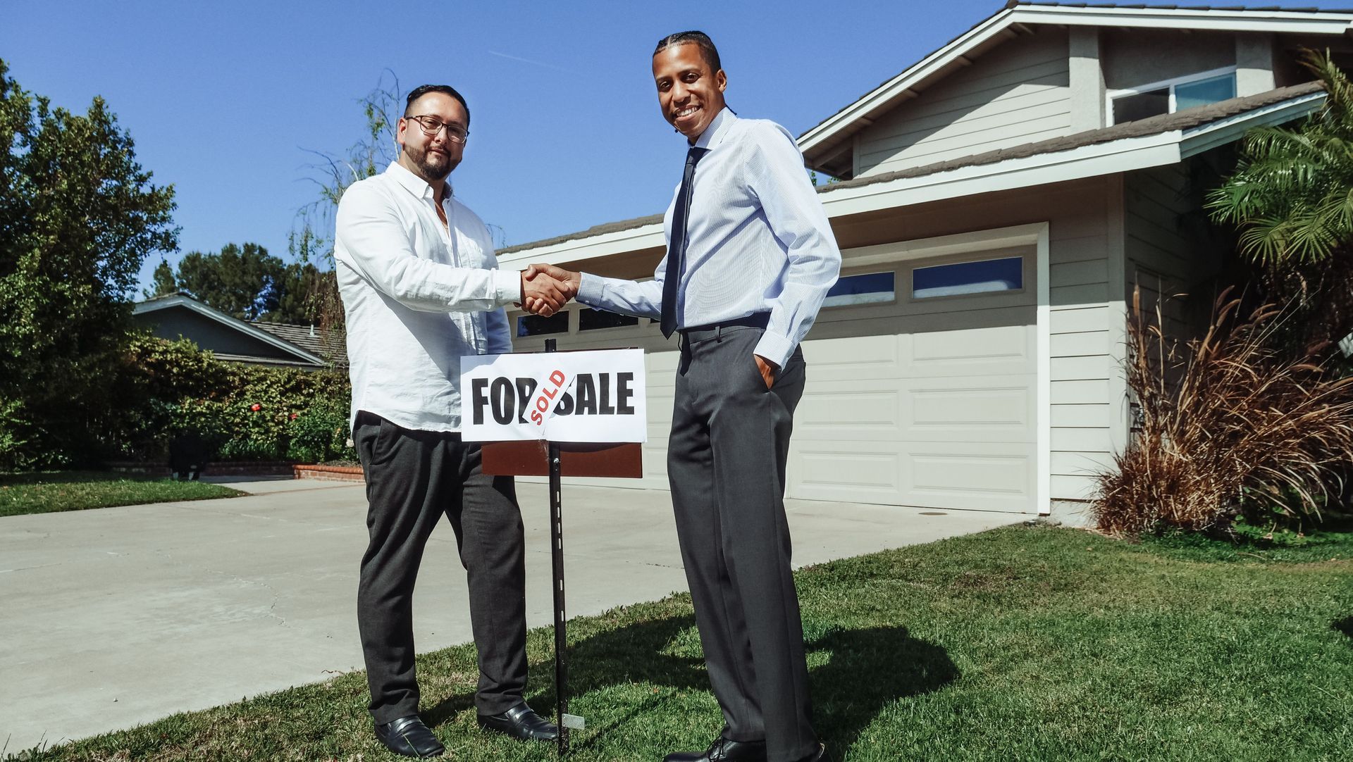 Realtor shaking client's hand in front of a for sale sign